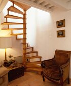 Antiker Plüschsessel unter hölzerner Wendeltreppe und weisser Holzbalkendecke in Landhaus-Wohnzimmer