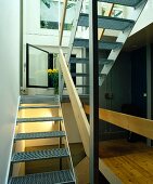 Geöffnetes Fenster hinter moderner Stahltreppe mit Gitterroststufen und Holzbrett als Geländer