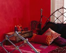 Rotes Schlafzimmer mit Kissen und Decke im indischen Stil auf Metallbett