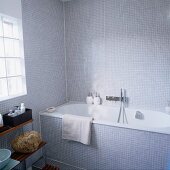 Badewanne mit Designer-Wandarmatur in Badezimmer mit hellgrauen Mosaikfliesen, Glasbausteinen