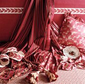 weiße, bemalte Porzellanschale auf rosé gemusterten Stoffen und Kissen vor Wand in dunkelrosa mit Tapetenbordüre