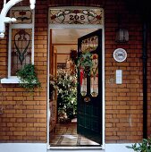 Geöffnete Hauseingangstür mit bunten Bleiglasfenstern und Weihnachtsschmuck in Backsteinhaus