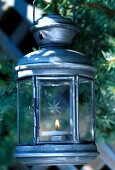 Weihnachtliches Windlicht aus Metall mit brennender Kerze vor Tannenzweigen