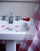 Rosenblätter schwimmen in einem Waschbecken mit verchromten Armaturen