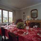 Festlich gedeckte Tafel mit roter Tischdecke, roten Tellern und Kristallgläsern in traditionellem Esszimmer
