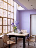 Moderne Holzstühle, die einen quadratischen Tisch umgeben, stehen vor einem großen Fenster des modernen violetten Esszimmers