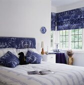 Blau-weiß gemusterte Jalousien, ein passendes Kopfteil und Kissen dienen als Farbtupfer in das in weiß gehaltene Schlafzimmer