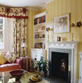Ein Vorhang mit einem blumigen Muster und einer roten Leiste setzt sich von den gelb gestreiften Tapeten und dem weißen Kamin ab