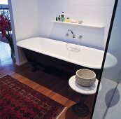 Eine schwarze freistehende Badewanne und ein orientalischer Teppich auf dem Parkettboden statten das weißgeflieste Badezimmer aus