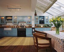 Riesige Wohnküche mit pastellblauer Landhaus-Einbauküche und Essplatz unter Schrägverglasung mit Sonnenschutz