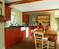 Rustikale Landhausküche mit rostroten Holzfronten und Deckenstrahlern über altem Kiefern-Esstisch mit cremefarbenen Holzstühlen