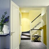 Geöffnete Tür mit Blick in ein gelbes Treppenhaus mit grauem Teppichboden