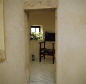 Blick in ein kleines Zimmer mit Fenster, weiss-gekacheltem Boden und Armstuhl