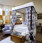 Schlafzimmer mit Himmelbett, blau-weiss gemusterten Bett-Vorhängen und mit Bambus-Innen-Fensterläden