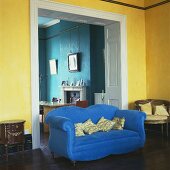 Blaues geschwungenes Sofa vor breitem Durchgang im gelb getönten Wohnzimmer
