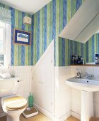Kleines Bad unter Dachschräge mit StandWC und – Waschbecken vor halbhoher weiss gefliester Wand und gestreifter Tapete