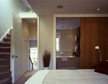 An open bedroom with a flight of stairs and an open door with a view into an en suite bathroom
