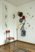 A metal chair with a red seat in the corner of a room next to hat collection on the wall