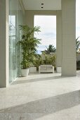An elegant entrance way with an upholstered bench and palms in front of the high glass doors