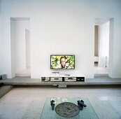 Ein Couchtisch aus Glas, ein niedriges Sideboard mit Multimediageräten und ein Flachfernseher an der Wand