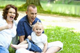 A happy young family sitting on the grass by a lake