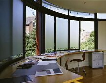 A modern home office with a built in desk in front of a curved window bank