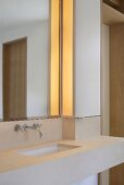 Scharfe Kanten im modernen Bad mit Beleuchtung neben Wandspiegel über minimalistischem Waschtisch