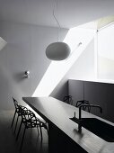 White hanging lamp above a breakfast bar with integrated sink and designer chairs