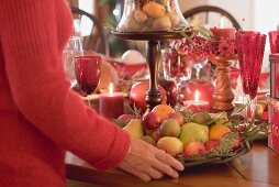 Woman placing bowl of fruit on table laid for Christmas