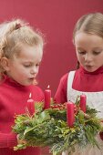 Zwei kleine Mädchen blasen Kerzen am Adventskranz aus