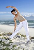 Frau macht Stretchübung am Strand (Südafrika)