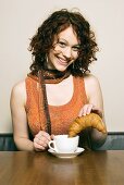 Woman dipping croissant into cup of coffee