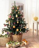 Weihnachtsbaum mit Schmuck in Obstform und mit Kerzen, davor Früchte in Körben auf dem Boden