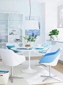A dining area in white with a round table, bucket chairs and touches of blue