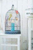 Candle in cage decorated with paper flowers and birds on outside