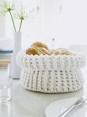 A white crochet bread basket filled with fresh rolls