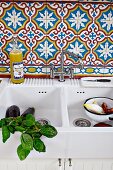 Weisses Keramik Spülbecken mit Basilikumzweigen und Gemüse, an Wand marokkanische Fliesen