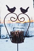 A tealight holder made from twigs on an iron stand decorated with birds