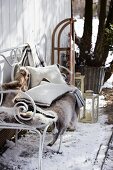 Rentierfell und Kissen auf einer Eisenbank im verschneiten Garten
