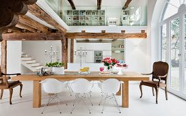 An open-plan dining room in white with a wooden beam ceiling and a glazed gallery