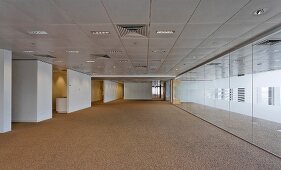 Reflective wall opposite white wall elements in wide corridor with coffer-style ceiling panels