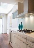 Blue vases on a white, modern, kitchen countertop with stainless steel pulls and exhaust hood