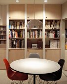 Round dining table and colored shell chairs in Bauhaus style in front of a built-in book shelf