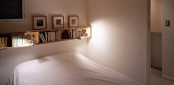 Narrow bookshelf of light wood above a bet with white linen