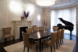 Dining table with upholstered chairs in Art Deco style in front of a grand piano in the bay window
