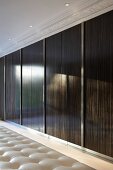 High gloss, wooden sliding doors and recessed ceiling spot lights in front of a stucco frieze in an elegant dressing room