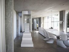 Weisses Treppenpodest vor Treppe im offenen Wohnraum mit Schalenstühlen aus Bauhauszeit vor Esstisch