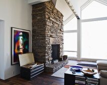 Rustic, natural stone fireplace next to a bank of windows