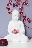 A Buddha figure holding an orchid in front of a wall decoration