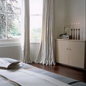 Candles burning in a modern bedroom with a cupboard next to the bay window